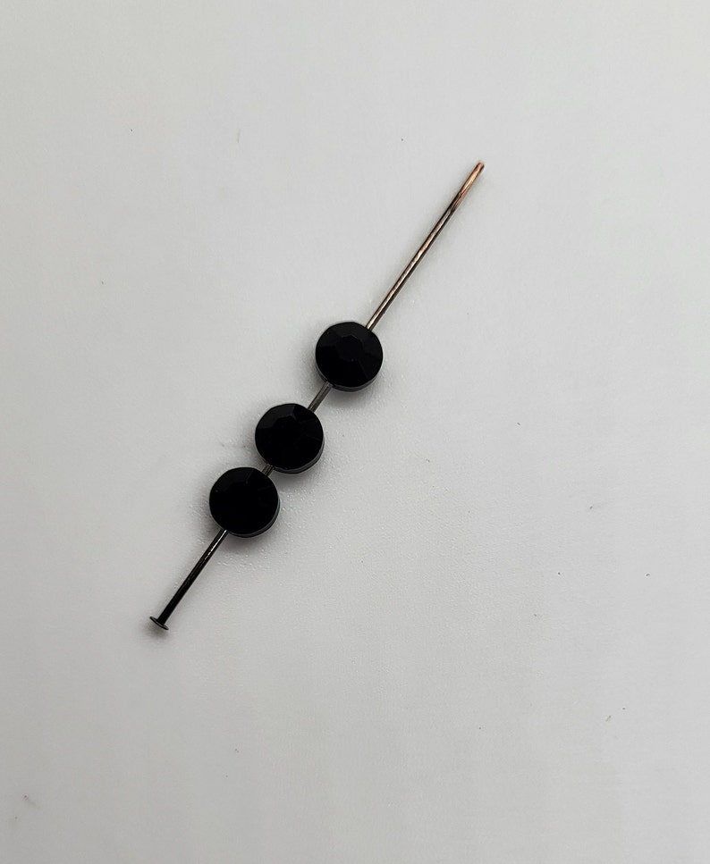 May include: Three black round beads threaded onto a silver wire.