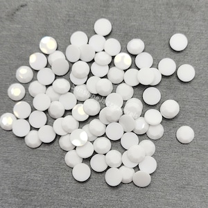 May include: A large group of white round rhinestones, scattered on a gray surface.