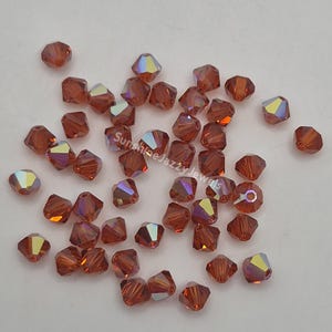 May include: A scattering of faceted, reddish-brown beads with iridescent highlights. The beads are small, with multiple facets that catch the light, creating a shimmering effect. The beads are likely for jewelry making or crafts.