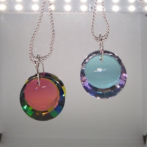May include: Two silver chain necklaces with round iridescent crystal pendants. One pendant is a light blue color and the other is a pink color.