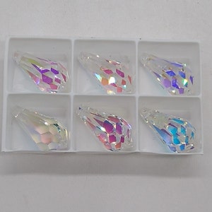 Könnte beinhalten: Sechs durchsichtige, regenbogenfarbene Glasanhänger in Tropfenform in einer weißen Kunststoffschale. Die Anhänger haben ein facettierten Design.