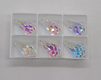 May include: Six iridescent clear glass teardrop-shaped pendants in a white plastic tray. The pendants have a faceted design.