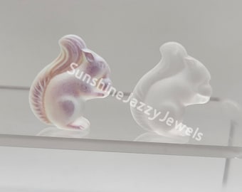 May include: Two small, white porcelain squirrel figurines. One squirrel is painted with purple and brown stripes on its tail. The other squirrel is plain white.