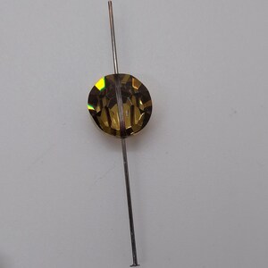 May include: A gold-toned, faceted, round bead is strung on a thin, silver-colored wire.