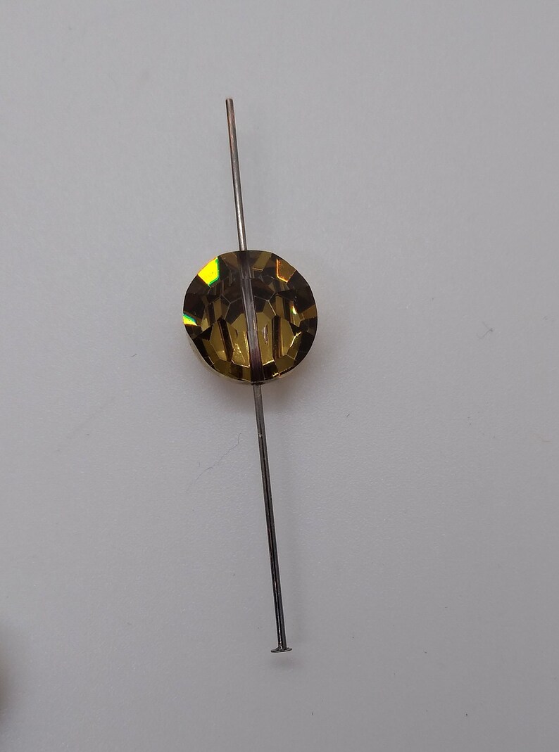 May include: A gold-toned, faceted, round bead is strung on a thin, silver-colored wire.