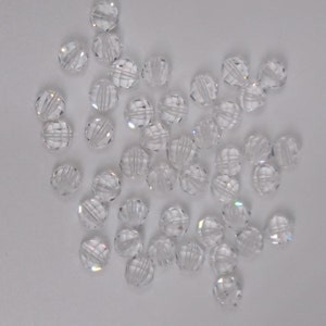 May include: A scattering of clear glass beads with a faceted design. The beads are round and have a slight iridescent shimmer.