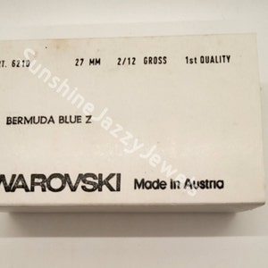 May include: A white box with black text that reads "ART. 6210 27 MM 2/12 GROSS 1st QUALITY BERMUDA BLUE Z SWAROVSKI Made in Austria".