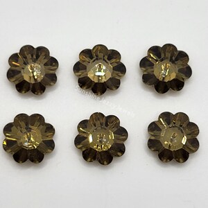 May include: Six brown flower-shaped rhinestones with a clear center. The rhinestones have a faceted design and are arranged in two rows of three.
