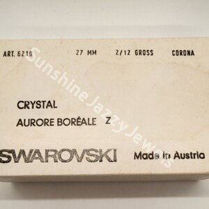 May include: A white box with black text that reads "SWAROVSKI Made in Austria" and "CRYSTAL AURORE BOR&Eacute;ALE". The box also has the text "ART. 6210", "27 MM", "2/12 GROSS", and "CORONA".