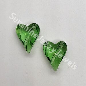 May include: Two green glass heart-shaped beads with a faceted design. The beads have a clear, shiny finish.