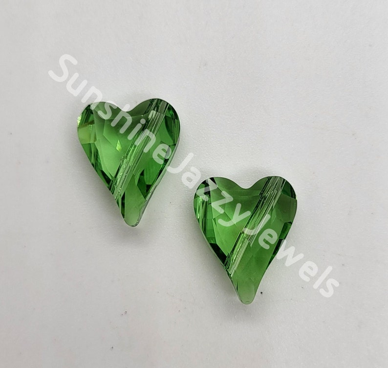 May include: Two green glass heart-shaped beads with a faceted design. The beads have a clear, shiny finish.