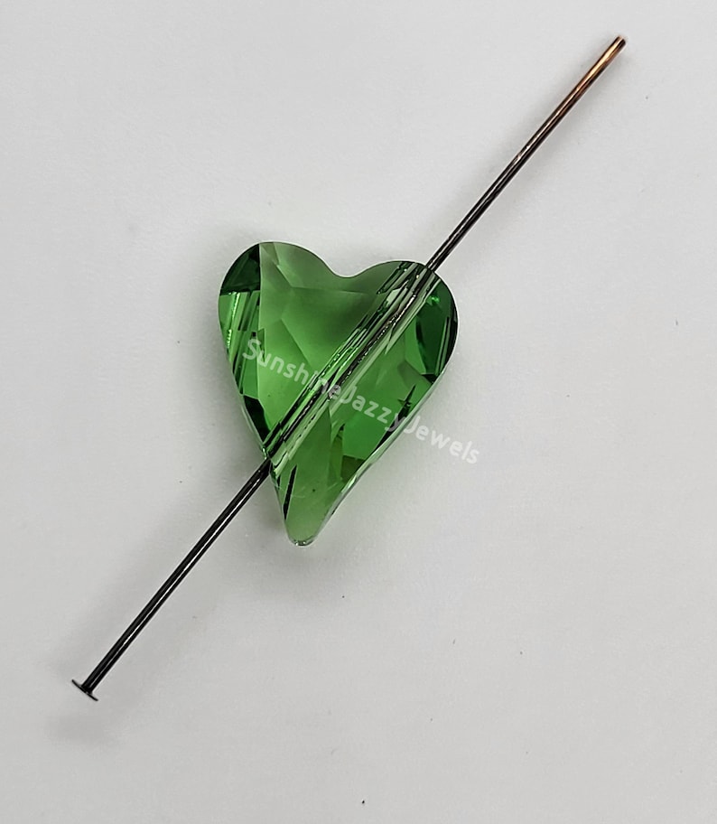 K&ouml;nnte beinhalten: Eine gr&uuml;ne Kristallherzperle mit einem Loch zum Aufziehen. Die Perle befindet sich auf einem d&uuml;nnen Metalldraht.