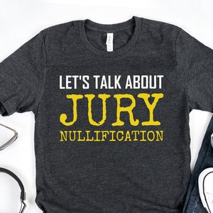 May include: A dark grey t-shirt with the text "Let's talk about Jury Nullification" in yellow lettering.