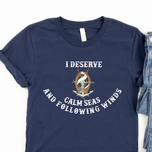 May include: Navy blue t-shirt with a white graphic of a ship's wheel and the text "I deserve calm seas and following winds".