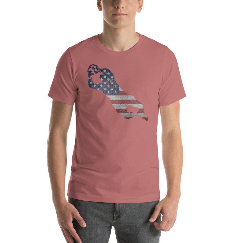 Puede incluir: Una camiseta roja con la silueta de un jugador de f&uacute;tbol americano atrapando una pelota. La silueta est&aacute; llena con la bandera estadounidense.