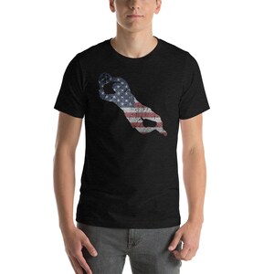 Puede incluir: Una camiseta negra con un dise&ntilde;o de bandera estadounidense desgastado en forma de mano haciendo el signo 'OK'.
