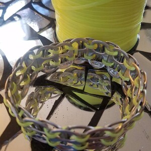 May include: A silver bracelet made from woven soda can tabs with neon yellow string woven through the tabs.