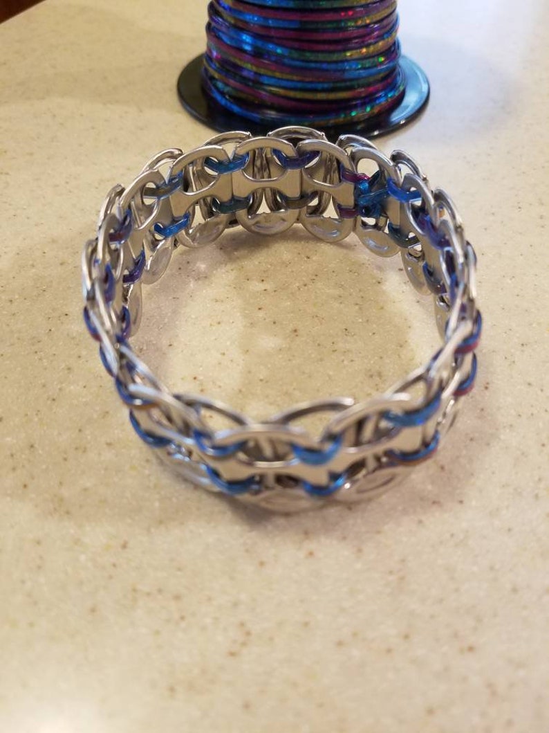 Peut inclure: Un bracelet argent&eacute; fait de languettes de tirage reli&eacute;es avec des accents bleus et violets.