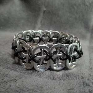 May include: A silver bracelet made from linked pull tabs with black string woven through the links.
