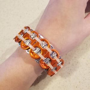 May include: A bracelet made from orange and silver pull tabs. The bracelet is woven together with white string.