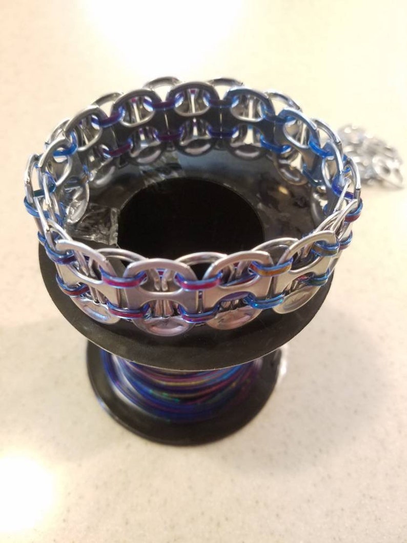 Peut inclure: Un bracelet argent&eacute; fait de languettes de canettes avec un cordon bleu et violet tiss&eacute; &agrave; travers les languettes.