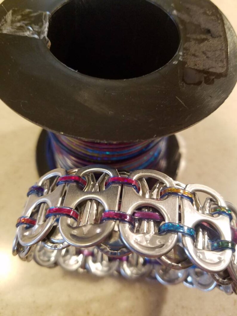 Peut inclure: Un bracelet argent&eacute; fait de languettes de canettes tiss&eacute;es ensemble avec du fil iridescent color&eacute;.