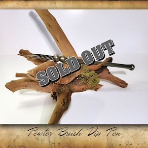 Puede incluir: Un bol&iacute;grafo de inmersi&oacute;n de pincel de peltre sobre un trozo de madera a la deriva con musgo. El bol&iacute;grafo es plateado y tiene un dise&ntilde;o retorcido. El texto "SOLD OUT" est&aacute; superpuesto a la imagen.