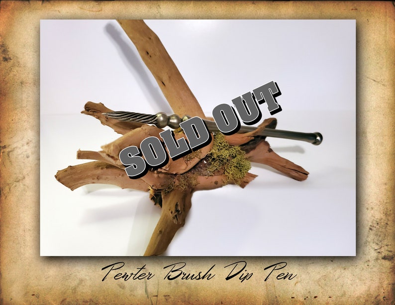 Puede incluir: Un bol&iacute;grafo de inmersi&oacute;n de pincel de peltre sobre un trozo de madera a la deriva con musgo. El bol&iacute;grafo es plateado y tiene un dise&ntilde;o retorcido. El texto "SOLD OUT" est&aacute; superpuesto a la imagen.