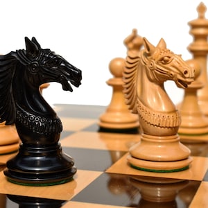 Peut inclure: Un jeu d'échecs noir et blanc avec les pièces de cavalier au premier plan. Le cavalier noir est sur une case claire et le cavalier blanc est sur une case foncée. L'échiquier est en bois avec un revêtement en feutre vert.