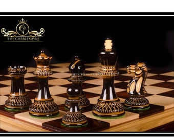 May include: A set of chess pieces with a black and gold design. The pieces are made of wood and have a glossy finish. The pieces are arranged on a wooden chessboard. The chessboard has a light brown and dark brown pattern. The text "THE CHESS EMPIRE" is visible in the top left corner of the image.