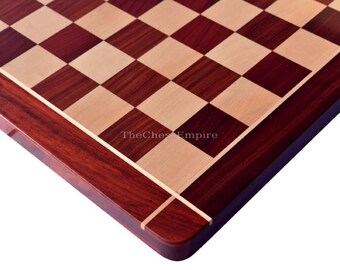 May include: Close-up of a wooden chessboard with a red mahogany and maple wood design. The board has a light brown border with a thin red line.