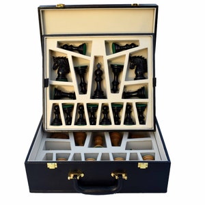 May include: A black chess set with a navy blue case. The chess pieces are black with green felt bottoms. The case is open, revealing the pieces in a fitted compartment. The bottom compartment holds wooden pieces. The case has a handle and gold-colored clasps.