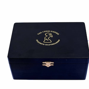 Puede incluir: Una caja de madera negra con un cierre dorado y un logotipo dorado que dice "The Chess Empire Exquisite Craftsmanship".