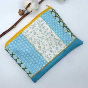 May include: A patchwork zipped pouch featuring various blue patterns, including polka dots and floral designs. The pouch has a yellow zip and trim, and a solid teal blue base. A stylish accessory for carrying small items.