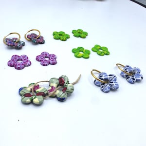 Peut inclure: Un assortiment de boucles d'oreilles et de perles faites à la main en forme de fleurs de différentes couleurs. Les boucles d'oreilles sont dotées de cerceaux dorés et de motifs floraux colorés. Les perles sont enfilées avec de la ficelle. La palette de couleurs comprend le violet, le vert, le bleu et le rouge.