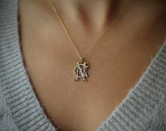 May include: A gold necklace with a delicate pendant featuring an intricate intertwined letter design.