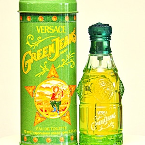 May include: A green Versace Green Jeans Man Eau de Toilette bottle and matching tin. The bottle is a unique shape with a green cap and base. The tin features the brand name and a graphic of a cowboy. The bottle contains 2.5 fl oz.