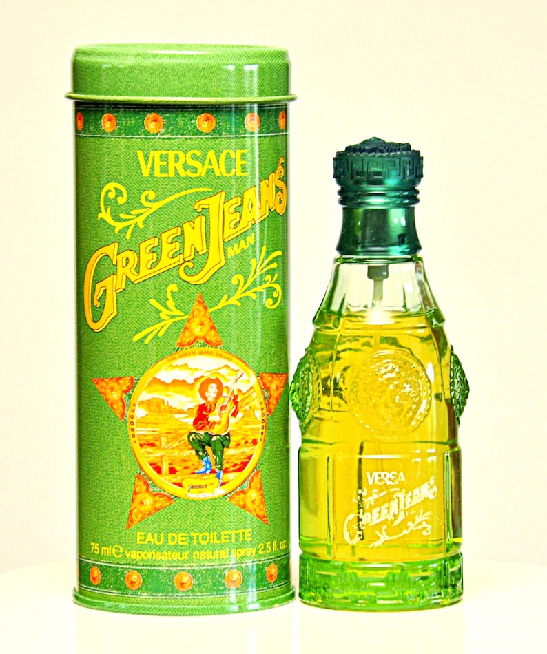 May include: A green Versace Green Jeans Man Eau de Toilette bottle and matching tin. The bottle is a unique shape with a green cap and base. The tin features the brand name and a graphic of a cowboy. The bottle contains 2.5 fl oz.