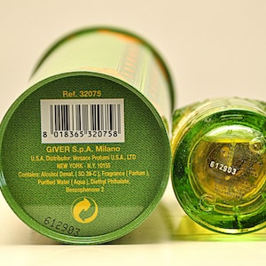 May include: A green perfume bottle and matching cylindrical container. The bottom of the bottle and the container's base are visible, displaying product information, including the reference number, barcode, and manufacturer details.