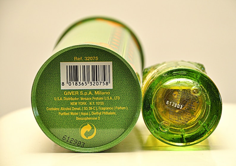 May include: A green perfume bottle and matching cylindrical container. The bottom of the bottle and the container's base are visible, displaying product information, including the reference number, barcode, and manufacturer details.