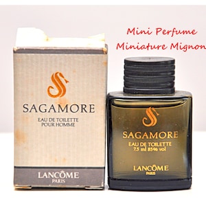 May include: Miniature bottle of Sagamore Eau de Toilette for men, 7.5 ml. The perfume bottle is dark with a black cap and a gold label. The box is beige with the Sagamore logo and text.