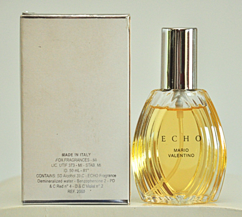 K&ouml;nnte beinhalten: Ein klares Glasfl&auml;schchen mit Echo-Parf&uuml;m von Mario Valentino. Das Fl&auml;schchen hat die Form einer Tr&auml;ne und einen silbernen Verschluss. Das Fl&auml;schchen steht auf einem wei&szlig;en Karton mit dem Markennamen und Produktinformationen.