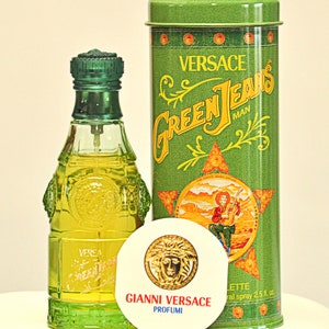 May include: A Versace Green Jeans Man fragrance set. The set includes a green glass perfume bottle, a green metal container, and a round white disc with the Versace logo. The container has the words "Green Jeans Man" in yellow.