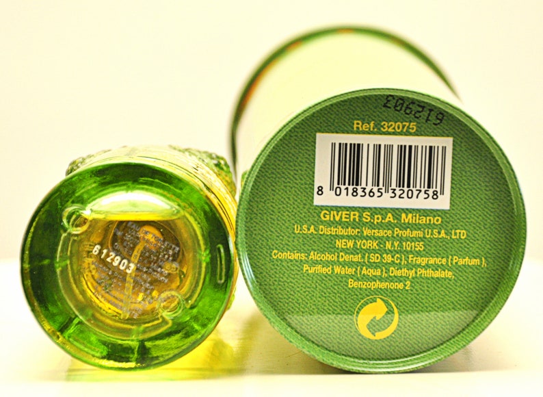 May include: A green glass perfume bottle with a textured design, next to a green and white cylindrical box. The bottle contains a yellow liquid. The box has a barcode and text that includes "GIVER S.p.A. Milano".