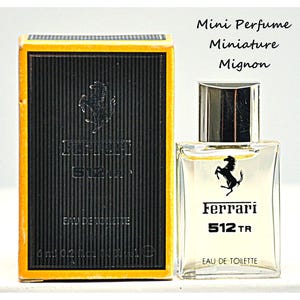 Op de afbeelding: Miniatuur Ferrari 512 TR Eau de Toilette parfumflesje en doos. De zwarte doos heeft een gele rand en het Ferrari-logo. Het transparante flesje heeft een zilveren dop en het Ferrari-logo. Bevat 6 ml.