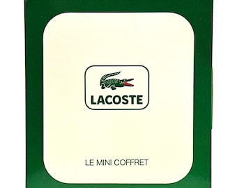 May include: A green and white box featuring the Lacoste logo, a green crocodile with a red mouth, inside a white rectangle. The text "LACOSTE" is below the logo. The words "LE MINI COFFRET" are printed at the bottom.