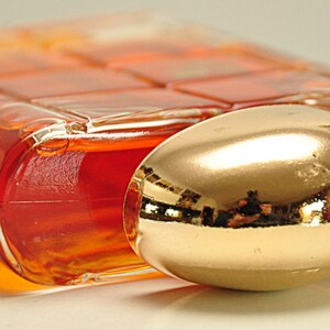 Puede incluir: Una botella de vidrio transparente con una tapa de color dorado. La botella est&aacute; llena de un l&iacute;quido naranja oscuro.