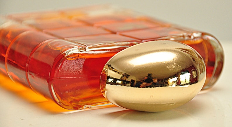 Puede incluir: Una botella de vidrio transparente con una tapa de color dorado. La botella est&aacute; llena de un l&iacute;quido naranja oscuro.