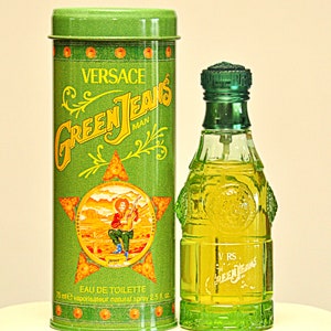 May include: A green Versace Green Jeans Man Eau de Toilette bottle and matching tin. The bottle is a unique shape with a green cap. The tin features the brand name and a graphic of a man playing a guitar. The bottle contains 2.5 fl oz.