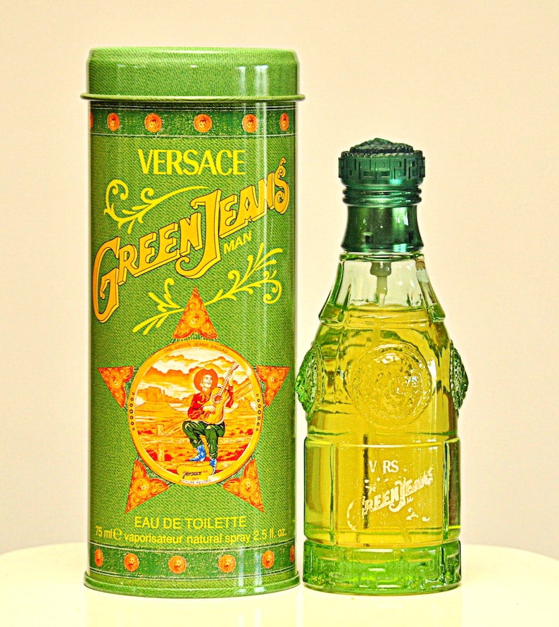 May include: A green Versace Green Jeans Man Eau de Toilette bottle and matching tin. The bottle is a unique shape with a green cap. The tin features the brand name and a graphic of a man playing a guitar. The bottle contains 2.5 fl oz.